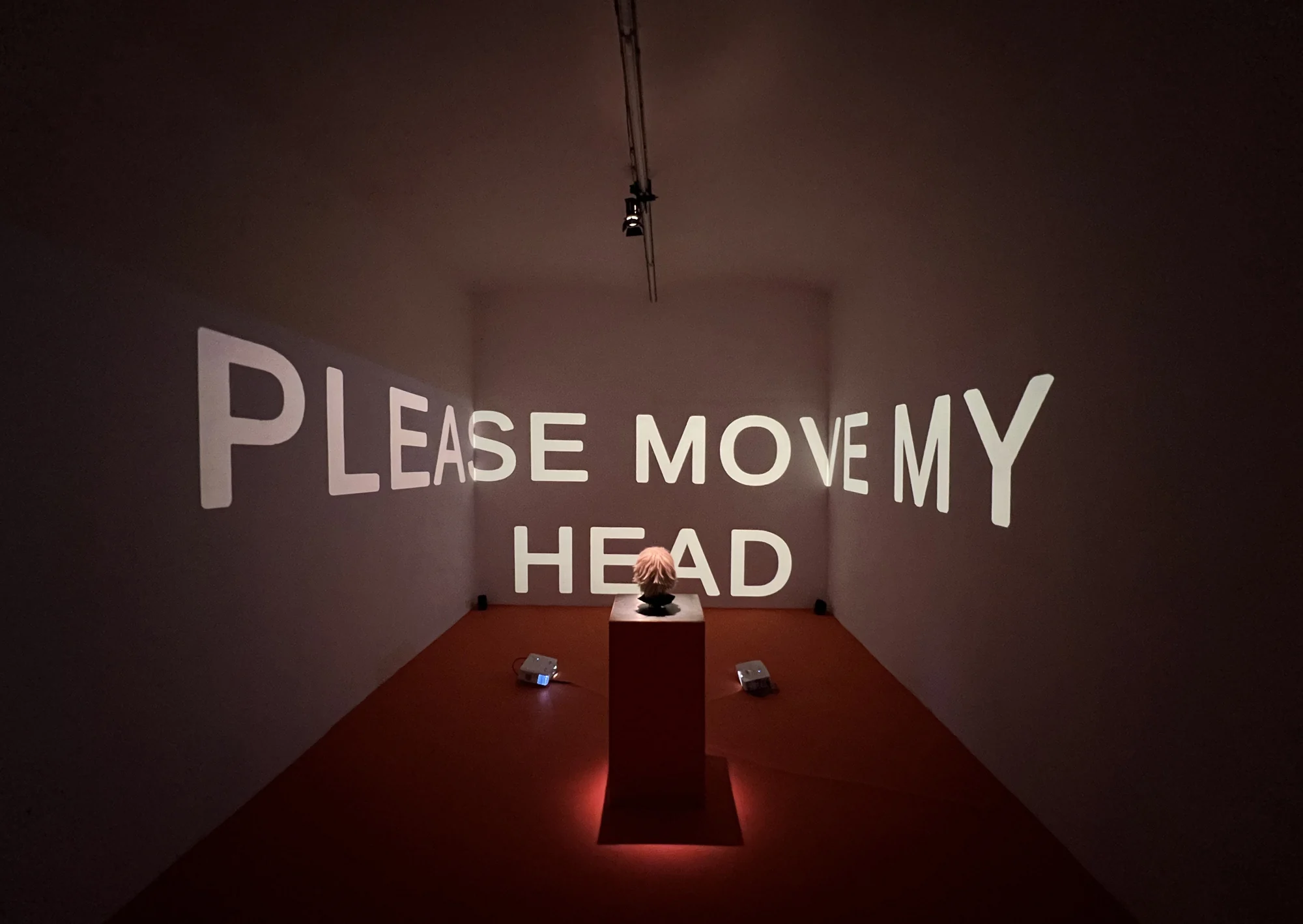 A head controller in a dark gallery beneath the projected words Please Move My Head